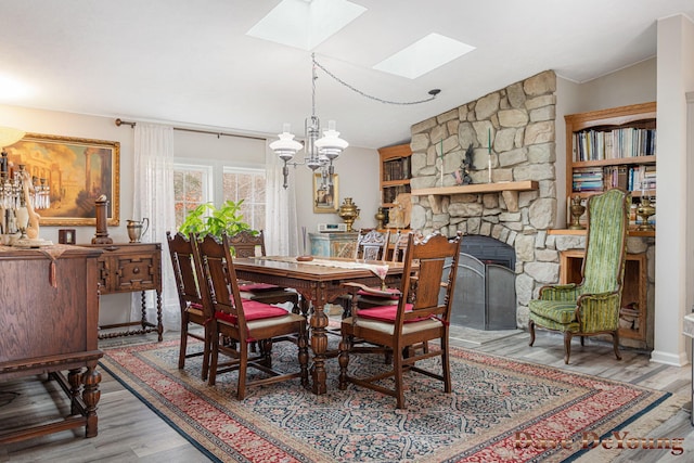 dining room with lofted ceiling with skylight, wood-type flooring, a fireplace, and a chandelier