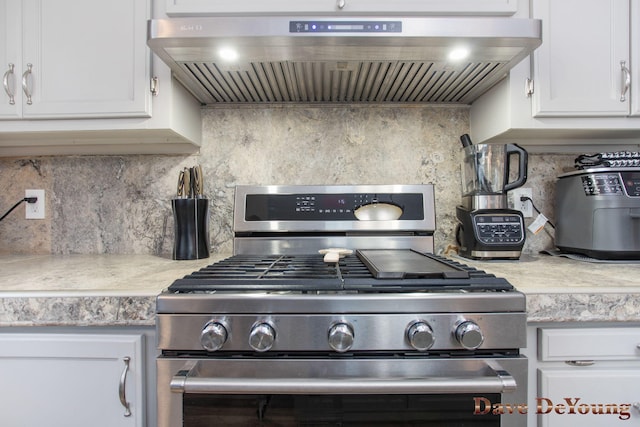 kitchen with decorative backsplash, stainless steel stove, white cabinetry, and wall chimney exhaust hood