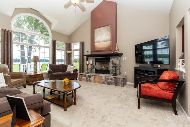 carpeted living room with a stone fireplace, ceiling fan, and high vaulted ceiling