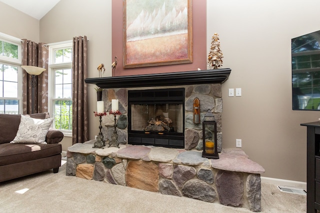 carpeted living room with a stone fireplace and lofted ceiling