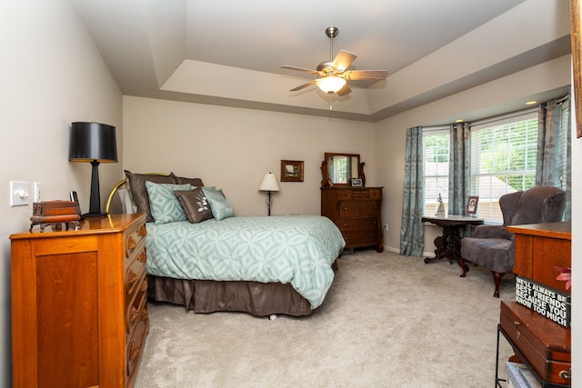 bedroom featuring light colored carpet, a raised ceiling, and ceiling fan