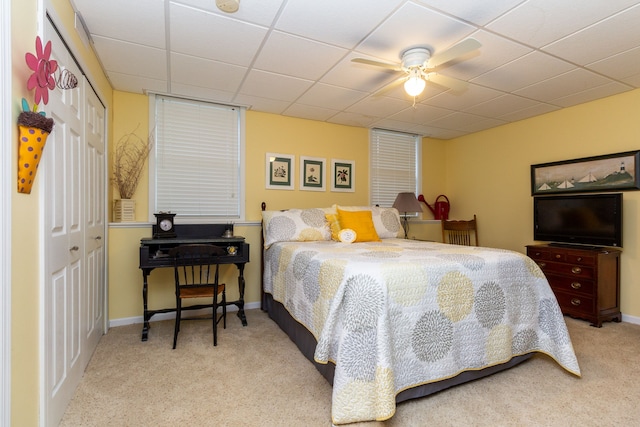 bedroom featuring a paneled ceiling, ceiling fan, a closet, and light colored carpet