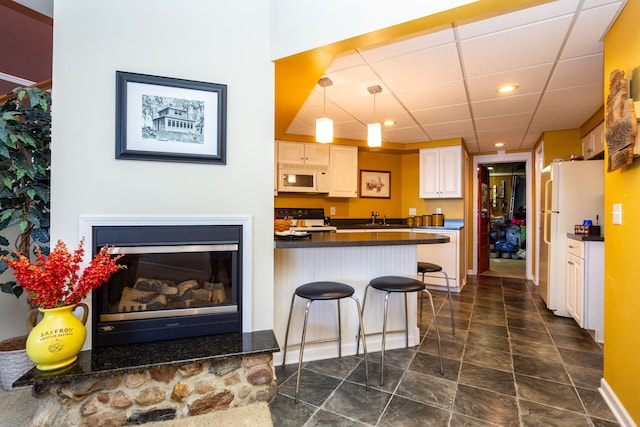 kitchen featuring a drop ceiling, white appliances, sink, a kitchen bar, and kitchen peninsula