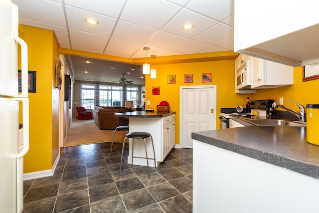 kitchen featuring white appliances, white cabinets, ceiling fan, a kitchen bar, and kitchen peninsula