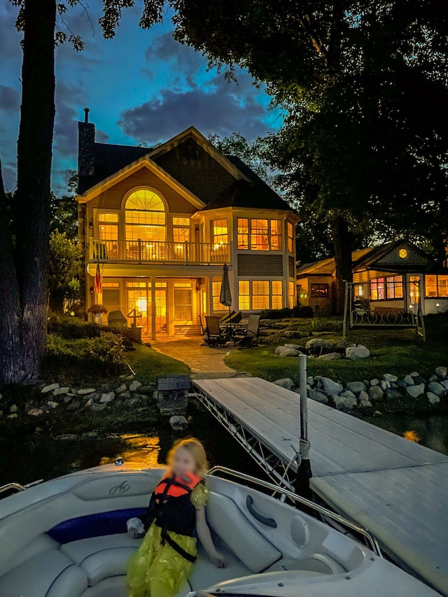 back house at dusk featuring a balcony and a patio