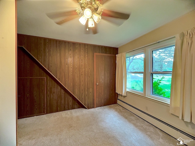 empty room with wood walls, ceiling fan, a baseboard radiator, and light carpet