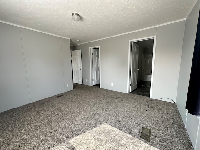 unfurnished bedroom with dark colored carpet, crown molding, a textured ceiling, and ensuite bath