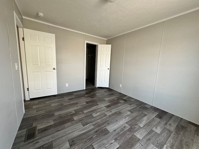 unfurnished bedroom featuring a textured ceiling, crown molding, a closet, and dark wood-type flooring