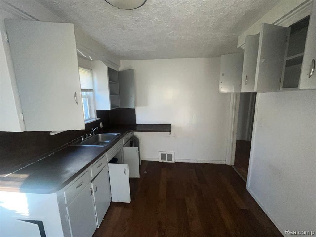 19613 Harned St, Detroit, MI 48234 - kitchen with a sink, dark wood-style flooring, dark countertops, a textured ceiling, and white cabinets