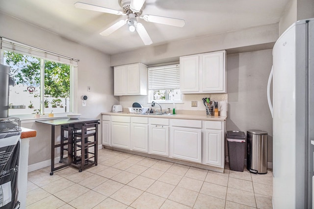 kitchen featuring light tile patterned floors, white refrigerator, white cabinetry, and sink