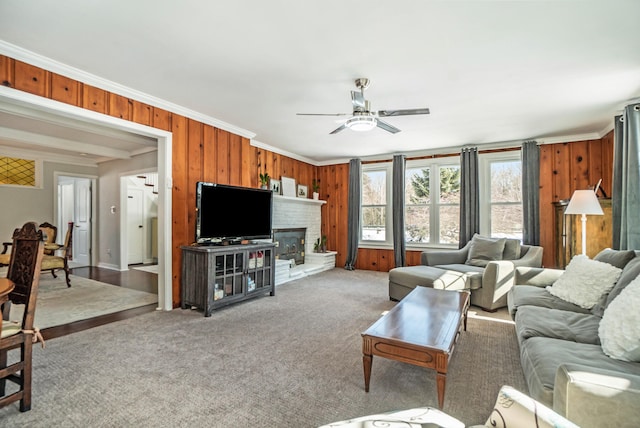 living room featuring crown molding, a fireplace, ceiling fan, and wood walls