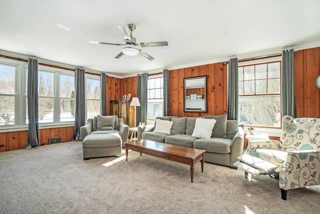 living room featuring wooden walls, ceiling fan, light colored carpet, and ornamental molding