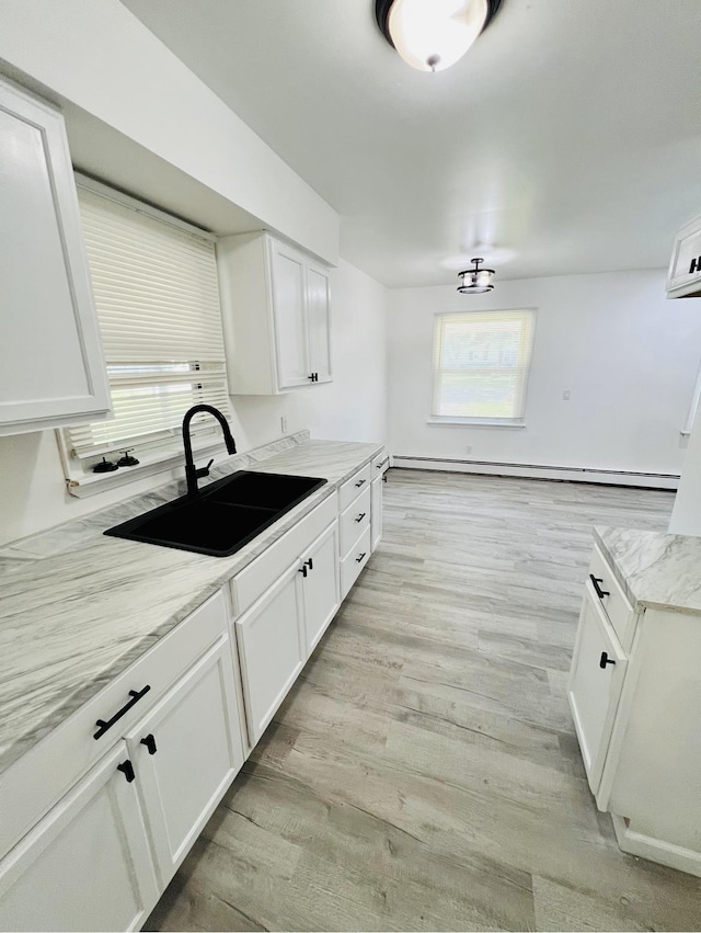 kitchen with light stone countertops, white cabinetry, a baseboard heating unit, sink, and light hardwood / wood-style flooring