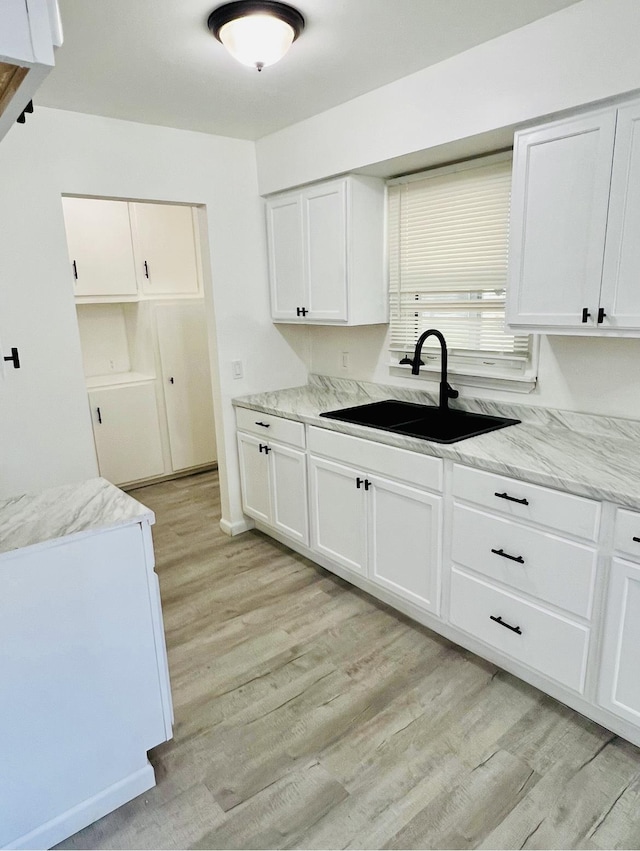 kitchen with light stone countertops, sink, white cabinets, and light hardwood / wood-style flooring