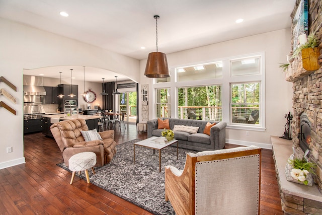 living room featuring dark hardwood / wood-style flooring, a stone fireplace, and a healthy amount of sunlight
