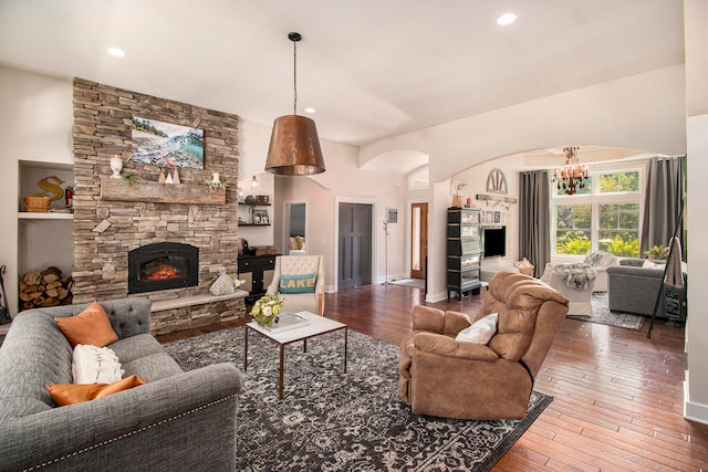 living room with an inviting chandelier, hardwood / wood-style flooring, and a stone fireplace