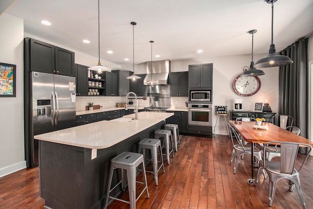 kitchen featuring pendant lighting, stainless steel appliances, an island with sink, and dark wood-type flooring