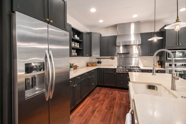 kitchen featuring wall chimney exhaust hood, dark wood-type flooring, stainless steel appliances, backsplash, and decorative light fixtures