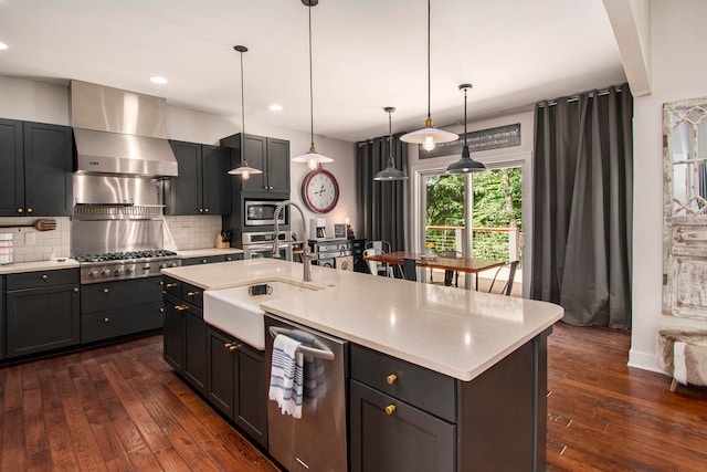 kitchen with wall chimney exhaust hood, stainless steel appliances, dark hardwood / wood-style floors, an island with sink, and pendant lighting