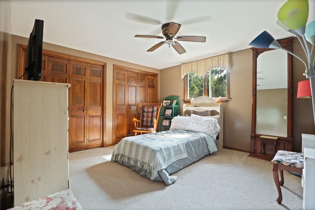 bedroom with ceiling fan, light carpet, and multiple closets