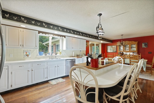 kitchen featuring sink, stainless steel dishwasher, pendant lighting, light hardwood / wood-style floors, and white cabinets