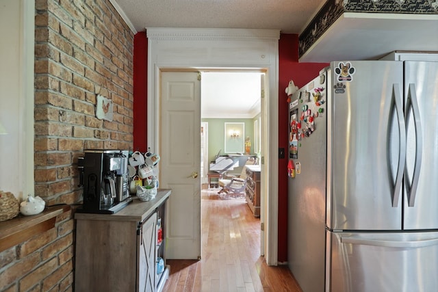 kitchen featuring stainless steel fridge, light wood-type flooring, crown molding, and brick wall