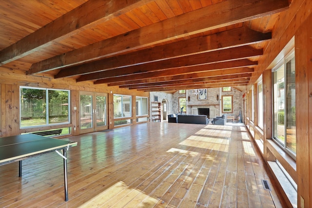 unfurnished sunroom featuring beamed ceiling, a stone fireplace, and plenty of natural light