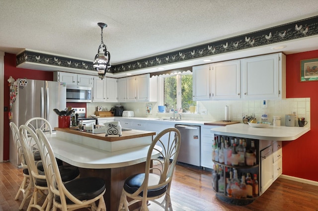 kitchen featuring appliances with stainless steel finishes, tasteful backsplash, decorative light fixtures, hardwood / wood-style floors, and white cabinetry