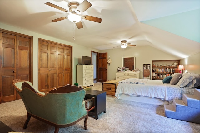 bedroom featuring ceiling fan, vaulted ceiling, light colored carpet, and two closets