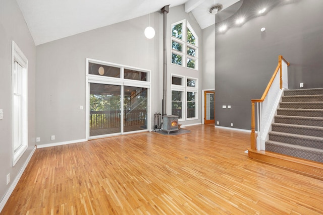 unfurnished living room with hardwood / wood-style flooring, a wood stove, and high vaulted ceiling