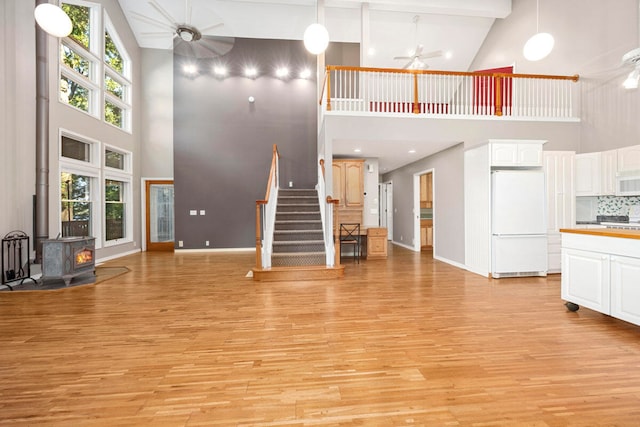 unfurnished living room with a wood stove, high vaulted ceiling, ceiling fan, beam ceiling, and light hardwood / wood-style floors