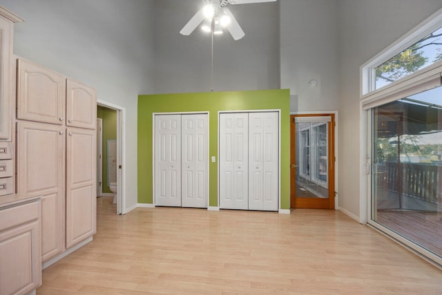 unfurnished bedroom with ceiling fan, a high ceiling, access to outside, two closets, and light wood-type flooring