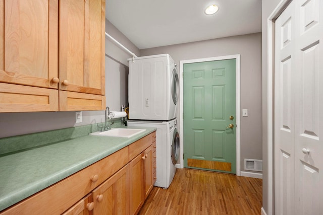 laundry area featuring stacked washer / drying machine, cabinets, sink, and light hardwood / wood-style flooring