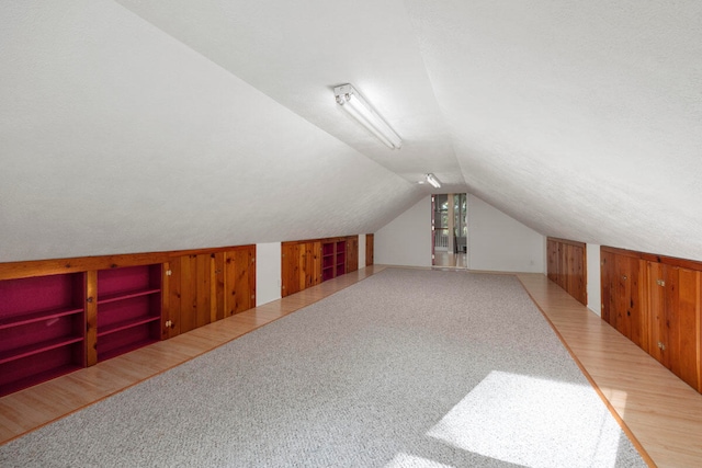 additional living space with a textured ceiling, wood walls, wood-type flooring, and lofted ceiling