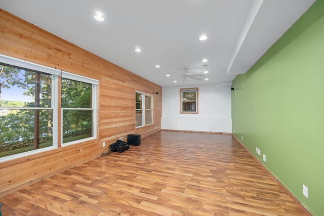 unfurnished living room featuring ceiling fan, light wood-type flooring, and wooden walls