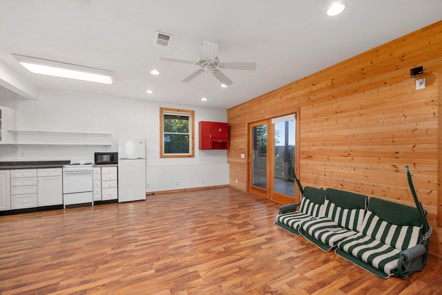 living area featuring ceiling fan, light hardwood / wood-style floors, and wooden walls