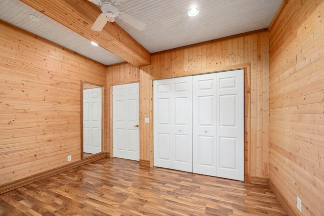 unfurnished bedroom with wood walls, ceiling fan, and wood-type flooring