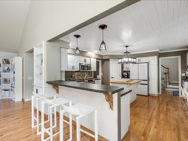 kitchen featuring white cabinetry, hanging light fixtures, kitchen peninsula, light hardwood / wood-style floors, and appliances with stainless steel finishes