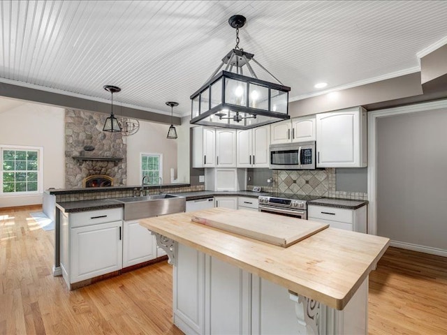 kitchen featuring stainless steel appliances, wooden counters, kitchen peninsula, pendant lighting, and white cabinets