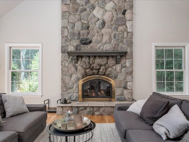 living room featuring wood-type flooring, a stone fireplace, and lofted ceiling