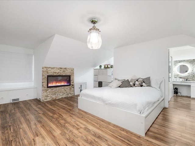 bedroom featuring a fireplace, hardwood / wood-style flooring, vaulted ceiling, and ensuite bathroom