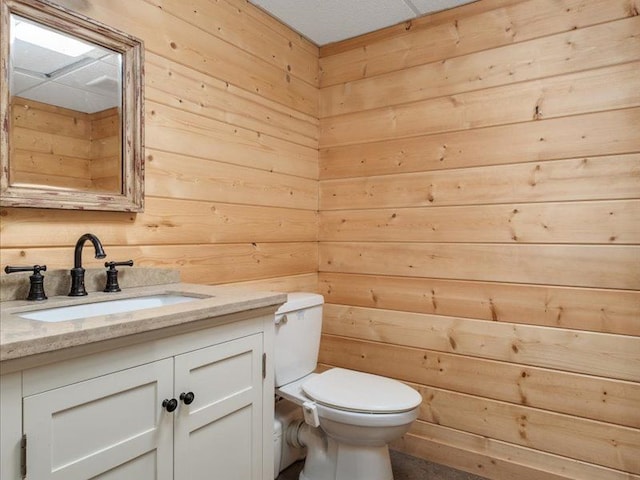 bathroom with vanity, toilet, and wood walls