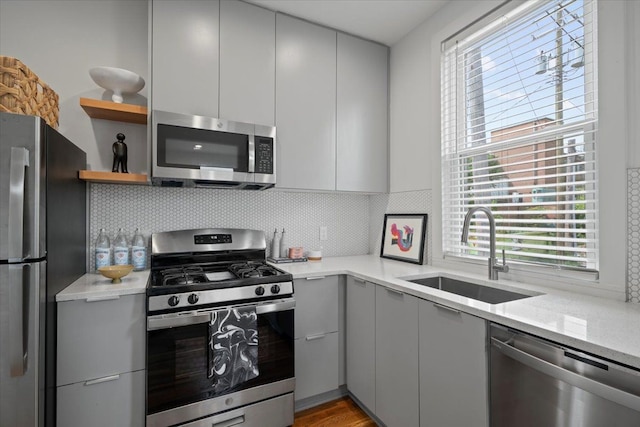 kitchen with light stone countertops, sink, gray cabinets, decorative backsplash, and appliances with stainless steel finishes