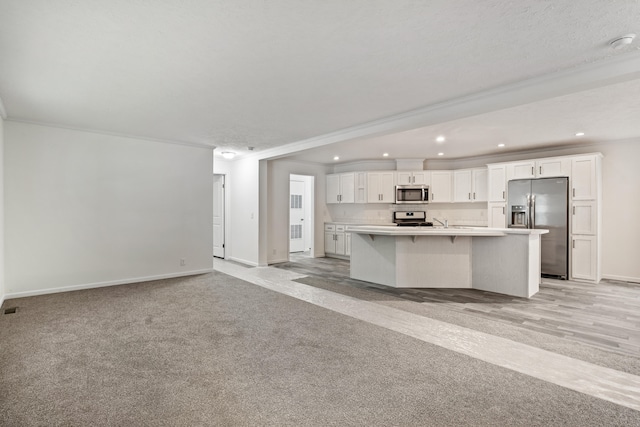 kitchen with white cabinetry, a kitchen island, stainless steel appliances, and light colored carpet