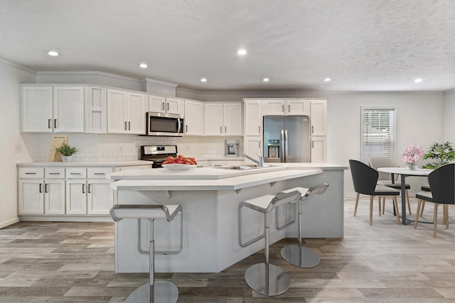 kitchen with white cabinets, a kitchen breakfast bar, stainless steel appliances, and a kitchen island with sink