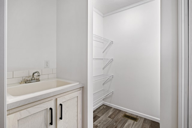 bathroom with hardwood / wood-style floors, a textured ceiling, crown molding, and sink