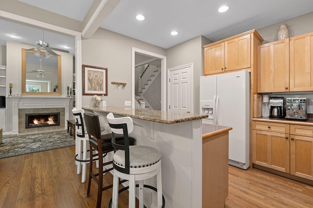 kitchen with a kitchen bar, light stone counters, a fireplace, light hardwood / wood-style floors, and white fridge with ice dispenser