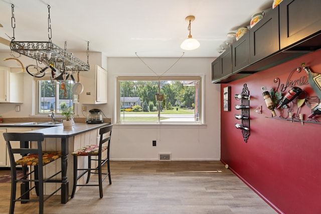 kitchen with white cabinetry, sink, pendant lighting, and light wood-type flooring