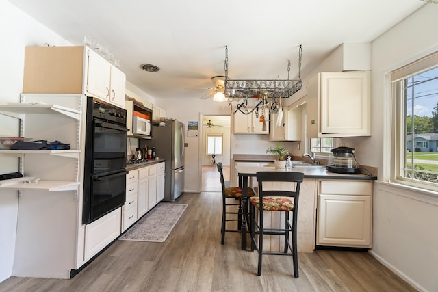 kitchen featuring sink, a breakfast bar area, ceiling fan, wood-type flooring, and stainless steel appliances