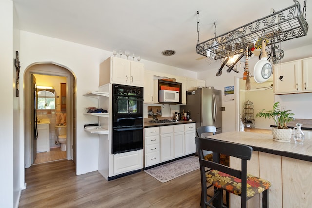 kitchen with double oven, white cabinets, dark wood-type flooring, and stainless steel refrigerator